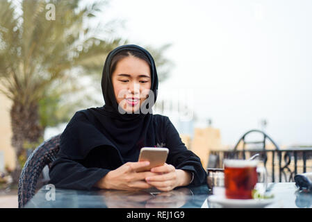 Muslimische Frau mit Phone bei einer Tasse Kaffee im Freien Stockfoto