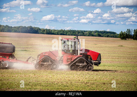 Landwirtschaftlichen Hintergrund mit roten Traktor Pflug ziehen, werfen Staub in der Luft. Mähdrescher im Weizenfeld. Schwere Maschinen während des Anbaus, der wor Stockfoto