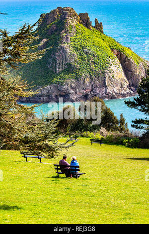 Ein paar sitzen auf einer Bank mit Blick auf das Meer und die Ansicht von Thatcher's Rock in Torbay. Stockfoto