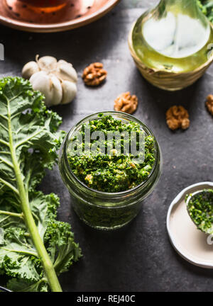 Grünkohl pesto in Glas auf dunklen rustikalen Küche Tisch Hintergrund mit Zutaten, Ansicht von oben. Kale Vorbereitung. Gesunde detox Gemüse. Eatin reinigen Stockfoto