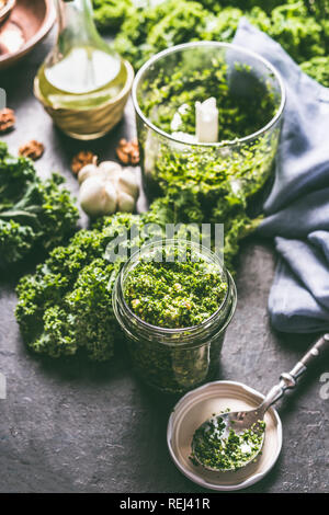 Raw Grünkohl essen Rezepte. Grünkohl pesto in Glas auf dunklen rustikalen Küche Tisch Hintergrund mit Zutaten, Ansicht von oben. Kale Vorbereitung. Gesunde detox Stockfoto