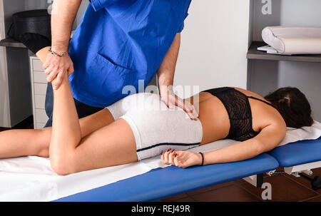 Männliche osteopath behandelt das Knie eines weiblichen Patienten mit Hilfe seiner Hände neu auszurichten und die Knochen der Gemeinsamen neu einstellen, wie sie auf einer Couch in seinem Nachteile liegt Stockfoto