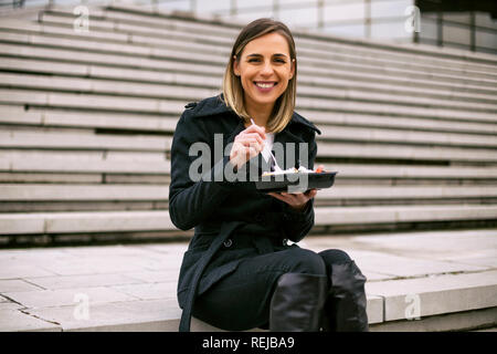 Schöne Geschäftsfrau genießt ruht auf einer Mittagspause beim Sitzen auf der Treppe in der Stadt. Stockfoto