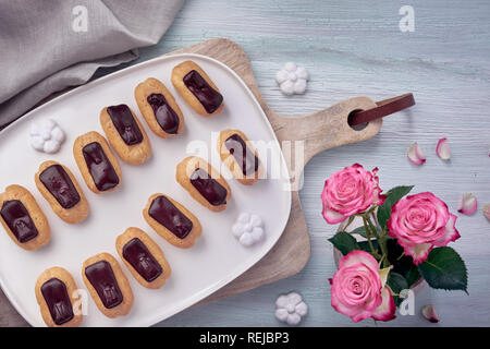 Mini Vanille eclairs mit Schokolade, Zuckerguß auf Licht strukturierten Hintergrund, Ansicht von oben Stockfoto