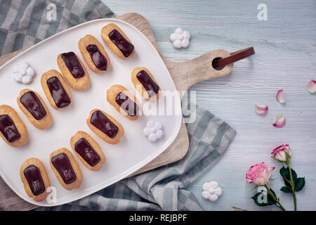 Mini Vanille eclairs mit Schokolade, Zuckerguß auf Licht strukturierten Hintergrund, Ansicht von oben Stockfoto