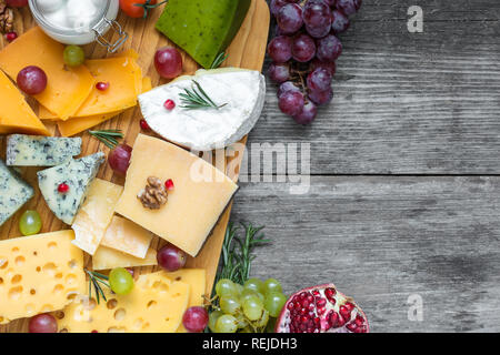 Verschiedene Käsesorten auf Holzbrett Teller serviert mit Walnüssen, Weintrauben, Granatapfel und Rosmarin auf rustikalem Holz Hintergrund, Ansicht von oben mit der Kopie Raum Stockfoto