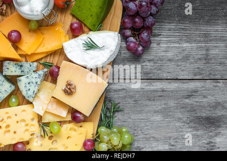 Verschiedene Arten von Käse auf Schneidebrett mit Trauben und Nüssen über rustikalen Holztisch, Ansicht von oben mit der Kopie Raum Stockfoto