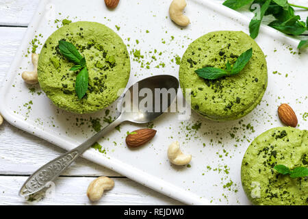 Green Matcha und Banane vegan rohe Kuchen mit Minze und Muttern über weiße Holztisch mit einem Löffel. Gesunde leckeres Essen. top View Stockfoto