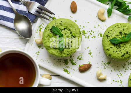 Green Matcha und Banane vegan raw Käsekuchen mit Minze und Muttern über weiße Holztisch mit Tasse Tee und Löffel. gesund leckeres Frühstück. nach oben v Stockfoto