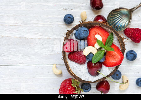 Vegan Kokosmilch Chia Samen Milchreis mit frischen Beeren, Nüsse und Minze über weiße Holztisch. gesundes Frühstück. nach oben anzeigen. Flach Stockfoto