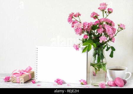 Schönen Blumenstrauß aus Rosen Blumen, Kaffeetasse, Makronen, Geschenkbox und leere weiße Grußkarte mit Platz für Text. Urlaub oder Hochzeit backgro Stockfoto