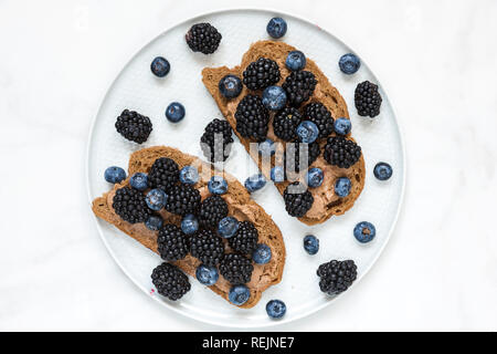 Vollkornbrot Toast mit Erdnussbutter, Heidelbeeren und Brombeeren auf weißem Marmortisch. gesundes Frühstück. top View Stockfoto