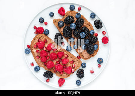 Gesundes Frühstück Toast für Kinder mit Peanut butter frische Beeren und Granatapfel Samen in einen Teller. top View Stockfoto