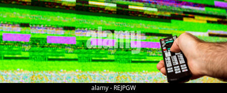 Mann mit großen TV-Fernbedienung, die versuchen, die das digitale Fernsehen Geräusche auf einem großen Plasma OLED 4 K Ultra HD High Dynamic Range HDR Smart TV zu beheben. Stockfoto