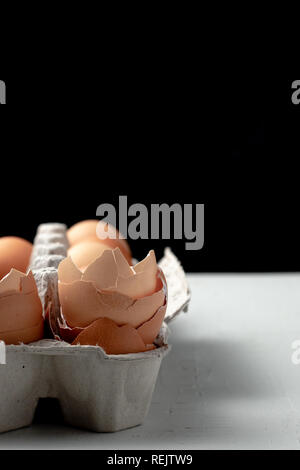 Gebrochene Eier im Karton auf schwarzem Hintergrund Stockfoto