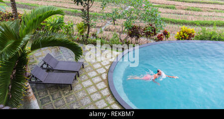 Luxus Resort. Man Relaxen im Pool Wasser. Schönen glücklichen gesunden männlichen Modell genießen Sommer Reisen Urlaub im Tropical Spa Hotel in Indonesien, Meerblick. Im Sommer entspannen Sie Konzept Stockfoto