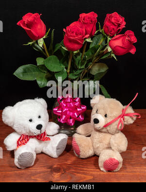 Zwei süße Kuschelige Teddybären mit roten Rosen in der Vase und rosa Schleife auf Holztisch auf dunklem Hintergrund. Valentinstag, Muttertag, Ostern, Weihnachten, Weddin Stockfoto