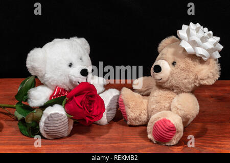 Zwei süße Kuschelige Teddybären mit einer roten Rose iand weißen Bogen auf Holztisch auf dunklem Hintergrund. Valentinstag, Muttertag, Ostern, Weihnachten, Weddin Stockfoto