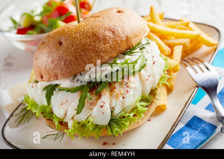 Gourmet Fisch Meeresfrüchte Burger mit Mayo und frischen Salat und Kräutern auf ein knuspriges Brötchen mit seitlichen Portion Pommes frites Stockfoto