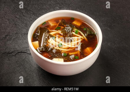 Ein Foto aus einer Schüssel miso shiru Suppe mit Tofu, Frühlingszwiebeln, Nudeln, und Wakame Algen, auf schwarzem Hintergrund Stockfoto