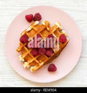 Traditionelle belgische Waffeln mit Himbeeren auf rosa Platte auf weißem Holz- Oberfläche, Ansicht von oben. Flach, Overhead, von oben. Close-up. Stockfoto