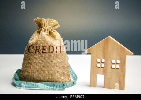 Ein Beutel mit Geld und einem Maßband und das Wort Kredit- und ein Holzhaus. Mangel an Geld, um das Darlehen zu zahlen. Hypothek für den Wohnungsbau. Einsparungen und accumulat Stockfoto