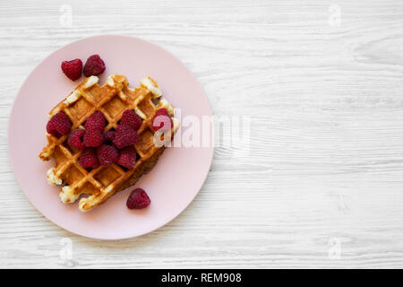 Traditionelle belgische Waffeln mit Himbeeren auf rosa Platte auf weißem Holz- Oberfläche, Ansicht von oben. Flach, Overhead, von oben. Kopieren Sie Platz. Stockfoto