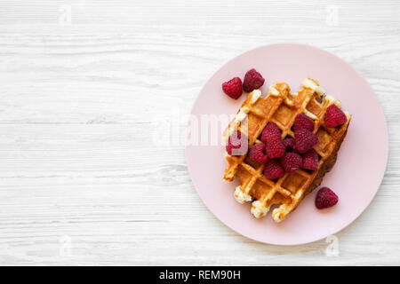 Traditionelle belgische Waffeln mit Himbeeren auf rosa Platte auf weißem Holz- Oberfläche, Ansicht von oben. Flach, Overhead, von oben. Close-up. Stockfoto