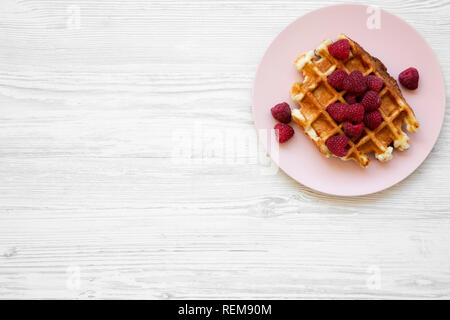 Traditionelle belgische Waffeln mit Himbeeren auf rosa Platte auf weißem Holz- Oberfläche, Ansicht von oben. Flach, Overhead, von oben. Kopieren Sie Platz. Stockfoto
