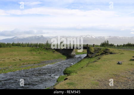 Brücke über Fluss mit Schnee und Bergen im Hintergrund in Island Stockfoto