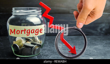 Glas Glas mit Münzen und die Inschrift 'Durch Hypotheken' und dem Pfeil nach unten. Weniger Interesse an der Hypothek. Niedrige Zinsen. Fallende Immobilienpreise. Stockfoto