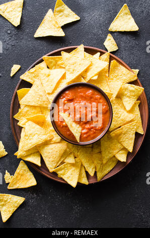 Nachos mais Chips mit pikanter Tomatensauce. Mexikanisches Essen Konzept. Gelber Mais totopos Chips mit Salsa Soße. Ansicht von oben.