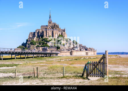 Der Mont Saint-Michel tidal Island in der Normandie, Frankreich, von den Salzwiesen gesehen mit einem hölzernen Tor und Zaun im Vordergrund unter blauem Himmel. Stockfoto