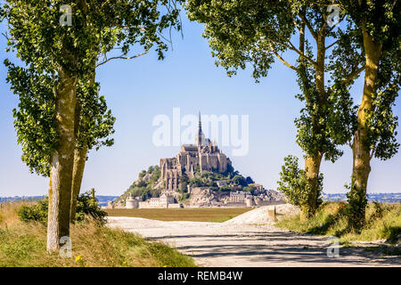 Der Mont Saint-Michel tidal Island in der Normandie, Frankreich, aus einem Feldweg mit Pappeln in den Poldern gesäumt unter einem hellen Sonnenlicht gesehen. Stockfoto