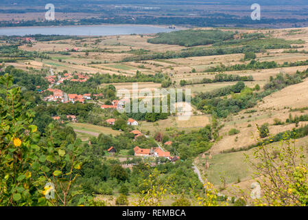 Schöne, frische Morgen im mittelalterlichen Bergdorf mit Kirche in der Mitte, neben der Wiese. Landwirtschaft in der Landschaft zwischen Hügeln und Dunkelgrün f Stockfoto