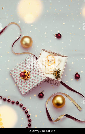 Verpackung Geschenk zu Weihnachten in die Box. Dekorieren mit Red Ribbon, roten Weihnachtskugeln und Tannenzweigen. Rosa Stoff im Hintergrund. Verwischt Weihnachten li Stockfoto