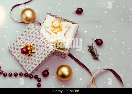 Verpackung Geschenk zu Weihnachten in die Box. Dekorieren mit Red Ribbon, roten Weihnachtskugeln und Tannenzweigen. Rosa Stoff im Hintergrund. Verwischt Weihnachten li Stockfoto