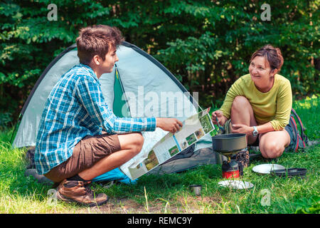 Verbringt einen Urlaub auf dem Campingplatz. Frau bereiten Sie eine Mahlzeit im Freien. Mann hält eine Karte. Planung nächste Reise. Stockfoto