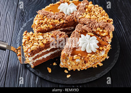 Erdnuss Kuchen gekrönt mit Kakao Peanut Butter, Sahne und Eischnee Rosen in Scheiben geschnitten auf einer Steinplatte auf einem Holztisch, Ansicht von oben, close-up Stockfoto