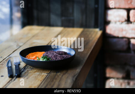 Vegan schwarzer Reis Schnitzel serviert mit orange Karotten mesh und microgreeens und koffeinfreien Kaffee. Vegetarische Nahrung hipster Cafe. Stockfoto