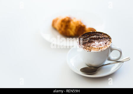 Cappuccino mit Schaumstoff in whilte Cup und Croissant auf weißem Hintergrund Stockfoto