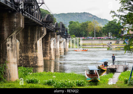 Kanchanaburi, Thailand - 18. August 2018: Die Brücke am Kwai (Khwae Yai), Boote auf dem Fluss und einem kleinen Pier neben einem Rasen. Stockfoto