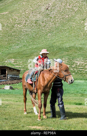 Kirgisische Mann sein Mädchen auf einem Pferd zu helfen, Sary Jaz Tal, Issyk-kul-region, Kirgisistan Stockfoto