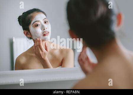 Frau mit Gesichtsmaske vor dem Badezimmerspiegel. Schöne weibliche tun Beauty Behandlung im Badezimmer. Stockfoto