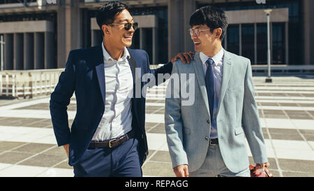 Zwei erfolgreiche Geschäftspartner zusammen gehen im Freien. Koreanische Geschäftsleute gehen gegen Bürogebäude. Stockfoto