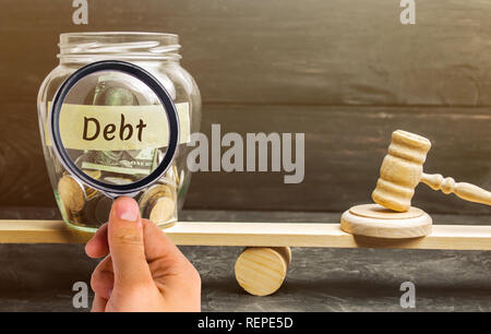 Ein Glas Glas mit Münzen und die Inschrift 'Debt" und "der Richter hammer sind auf der Waage. Konzept der finanziellen Krise und Problemen. Risk Management Stockfoto