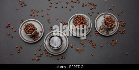Kaffee und Kaffeebohnen in Glas Tassen mit sausers, auf Schwarz Farbe Hintergrund, Ansicht von oben Stockfoto