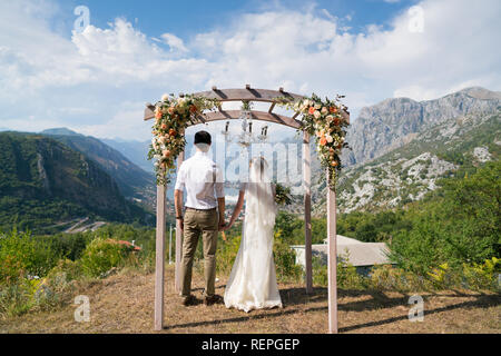 Das Brautpaar steht unter der eingerichteten Arch und Blick auf die Bucht Hand in Hand Stockfoto