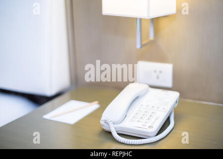 Hotel Schlafzimmer weißes Telefon auf dem Nachttisch mit Notizblock und Bleistift eine Nachttischlampe und Steckdose alle in einem hellen Szene Stockfoto