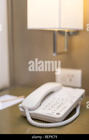 Hotel Schlafzimmer weißes Telefon auf dem Nachttisch mit Notizblock und Bleistift eine Nachttischlampe und Steckdose alle in einem hellen Szene Stockfoto